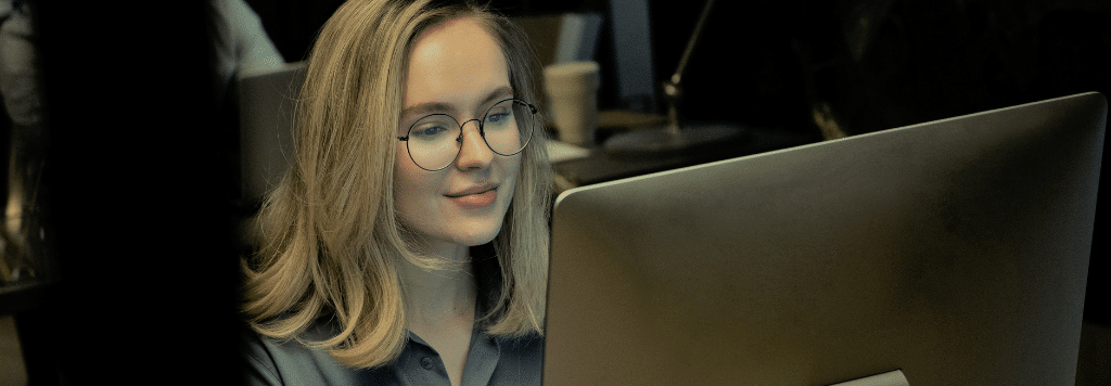 professional woman in glasses smiles while looking at computer screen