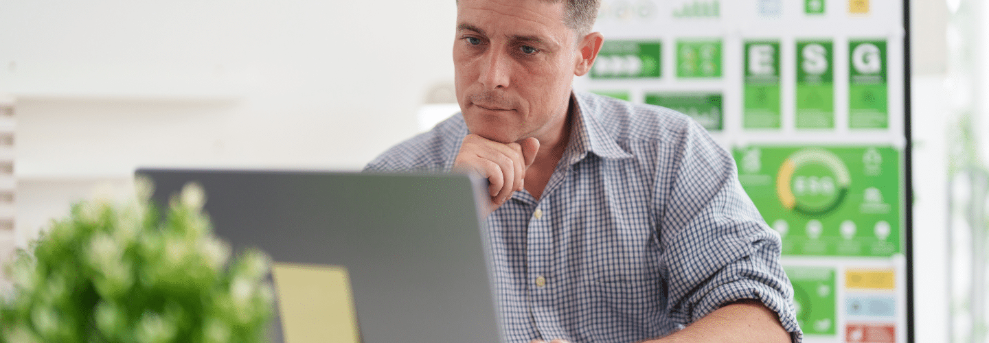 man looks at computer laptop screen with chin on hand