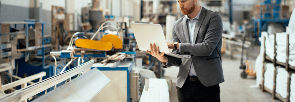 Man in Factory, Dressed Professionally, on a Laptop